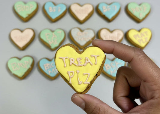 Heart-shaped dog cookie with 'I love you' text held by a hand, with more cookies in the background by TheDogBFF Barkerie